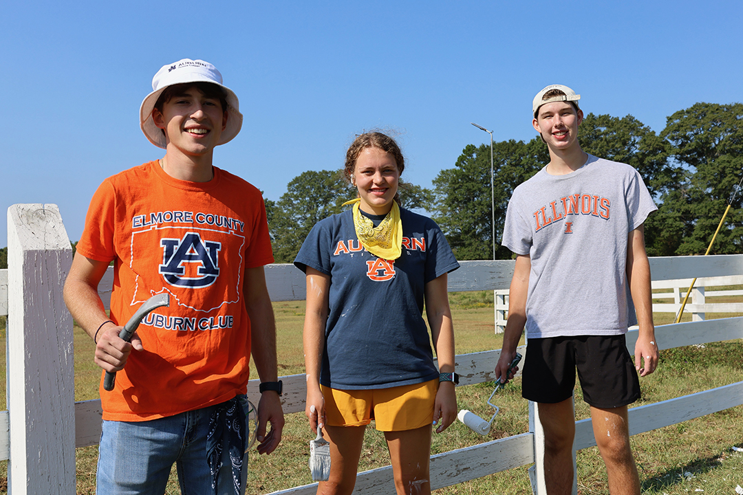 three students standing next to a fence they are painting